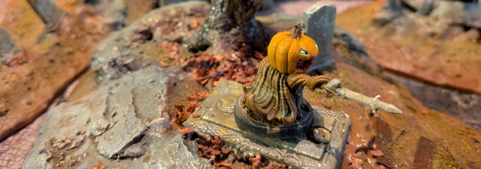 A tiny carved pumpkin-headed figure stands on a weathered stone base amid autumn leaves and rocky ruins