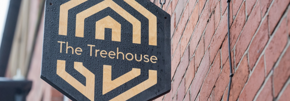 The Treehouse board game cafe outdoor sign on a brick wall, slightly wet from the rain
