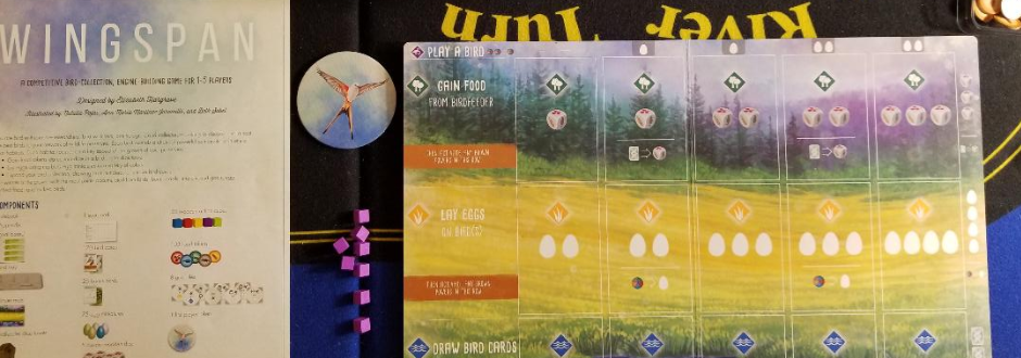 Board game components for "Wingspan." A player mat with spaces for actions sits beside instructions. Purple cubes and a bird token are nearby.