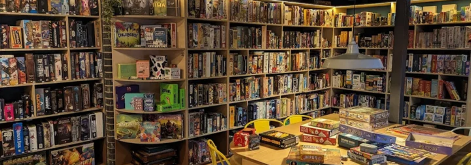 A collection of board games on shelves, with some laying across a table in the foreground