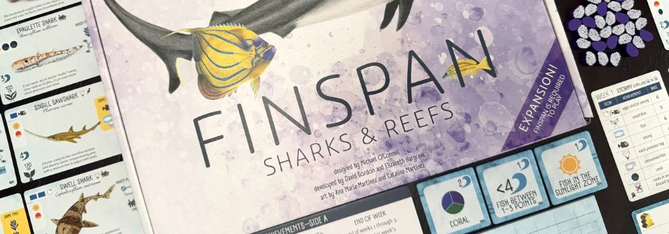 Box cover of a board game titled "Finspan: Sharks & Reefs" surrounded by cards and pieces. Features a shark and fish illustration, giving an aquatic theme.