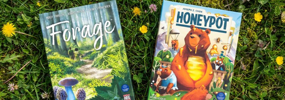 Forage and Honeypot board game boxes laying down on a grassy field with yellow flowers