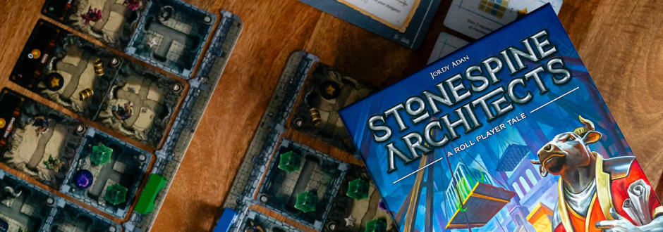 Board game on a wooden table featuring detailed map boards with colorful tokens and a box titled "Stonespine Architects" with vibrant artwork.