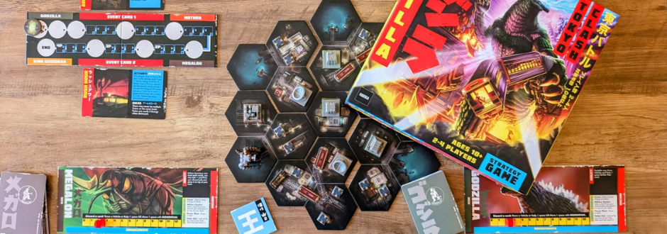 Godzilla: Tokyo Clash header image - game box and components spread out on a wooden table