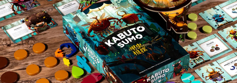 Board game "Kabuto Sumo" box on a wooden table surrounded by colorful game pieces and cards. The scene is vibrant and lively, conveying excitement.