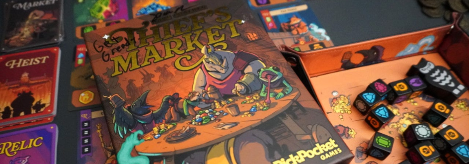 Board game setup featuring 'Thief's Market' box art with vibrant characters around a table of treasures. Colorful dice and game pieces scattered nearby. The scene conveys a playful and adventurous tone