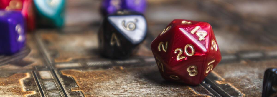 A close-up of colourful polyhedral dice, including a red 20-sided die, scattered on a tabletop game board.