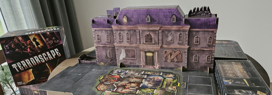 A purple haunted mansion miniature stands on a tabletop game board beside a horror-themed TerrorScape box