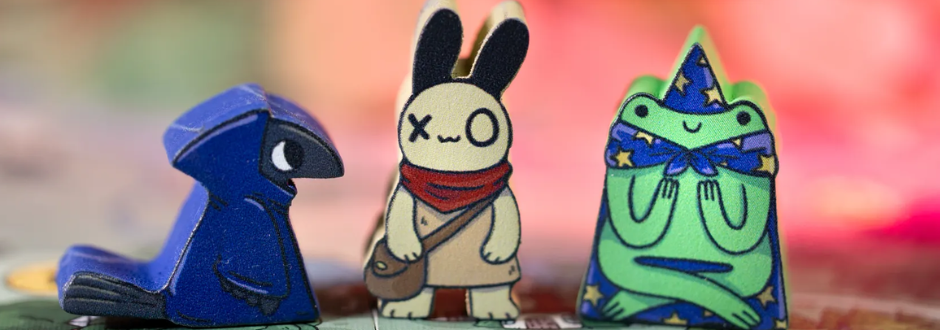 A close-up of three wooden character standees from “A Wild Venture,” featuring a blue bird, a rabbit with a scarf, and a frog dressed as a wizard.