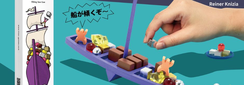 A hand places a metal cube onto a purple balancing ship filled with colorful blocks and figures. A cartoon speech bubble in Japanese adds playful tension.