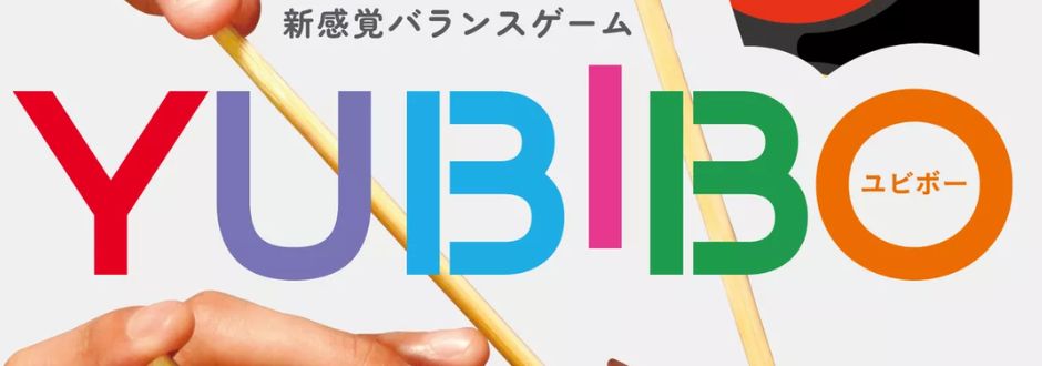 Two hands hold wooden sticks against a white background. The bold, colorful text "YUBIBO" overlays the image, conveying a playful, vibrant mood. Japanese characters are also present.
